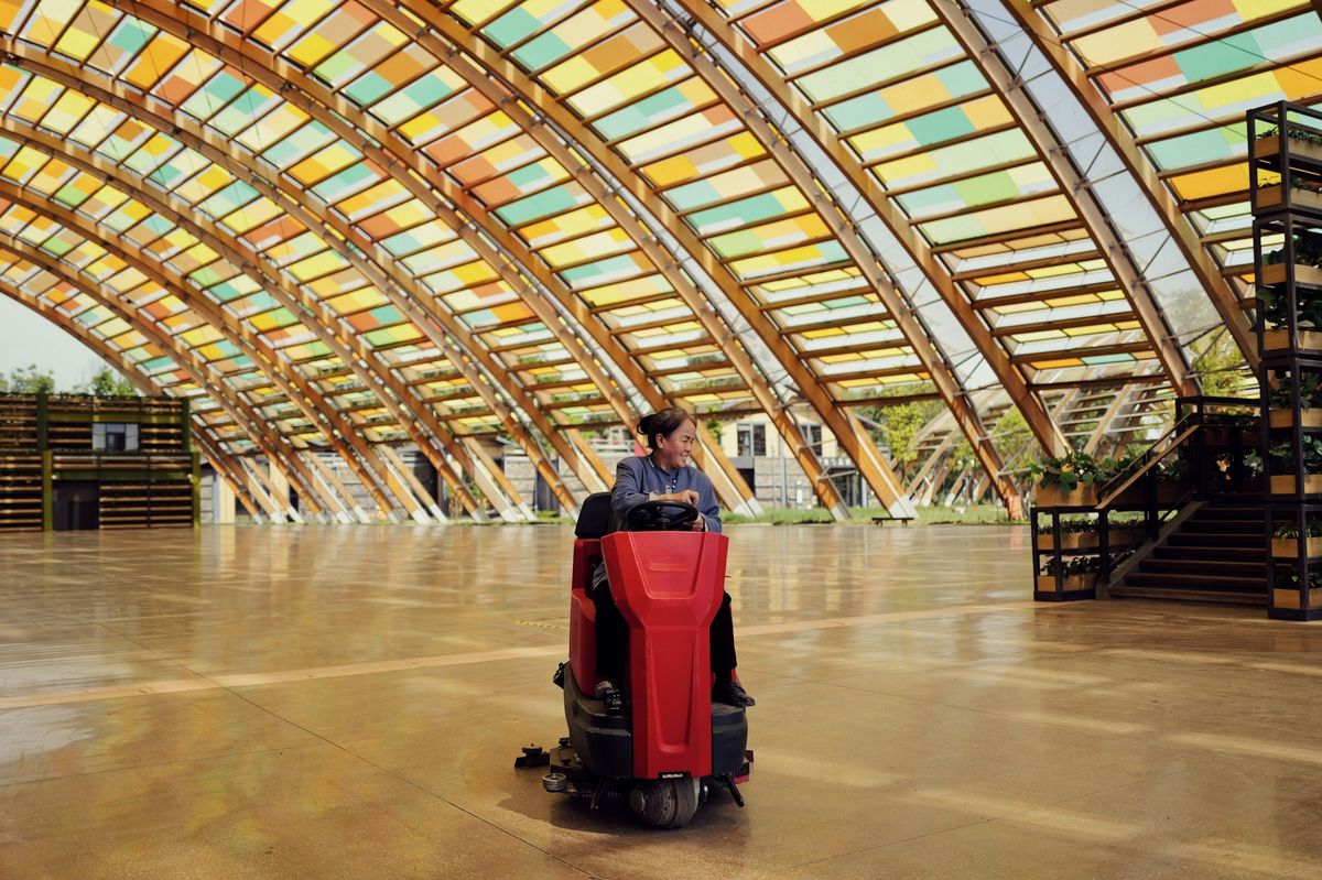 Een vrouw rijdt met een schrobmachine over de vloer van een grote hal